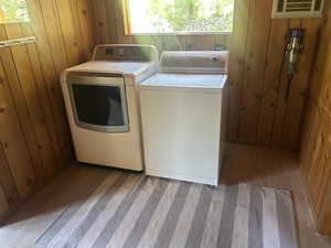 Laundry room with washing machine and dryer, wood walls, and a wall unit AC