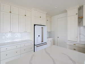 Kitchen featuring white appliances, decorative backsplash, light stone counters, and white cabinetry
