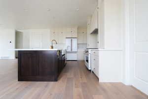 Kitchen with high end appliances, light wood-style flooring, white cabinetry, light countertops, and backsplash