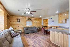 Living room featuring a ceiling fan, recessed lighting, a textured ceiling, wood walls, and wood finished floors