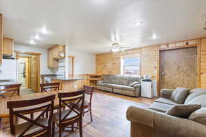 Living room with a textured ceiling, wood walls, ceiling fan, light wood finished floors, and recessed lighting