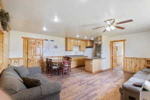 Living room with a textured ceiling, light wood-style flooring, wooden walls, wainscoting, and a ceiling fan