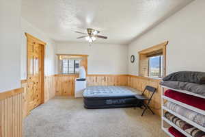 Carpeted bedroom with wainscoting, a textured ceiling, wooden walls, and a ceiling fan
