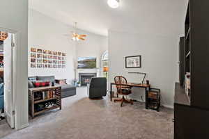 Carpeted office with vaulted ceiling, a ceiling fan, and a glass covered fireplace