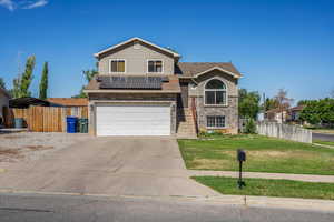 View of front of home with driveway, brick siding, a garage, solar panels, and a shingled roof