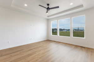 Unfurnished room featuring a raised ceiling, light wood-style flooring, recessed lighting, and ceiling fan