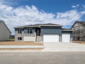 View of front of property with stone siding, an attached garage, concrete driveway, and roof with shingles