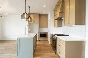 Kitchen with gas stove, light wood-style flooring, premium range hood, an island with sink, and recessed lighting