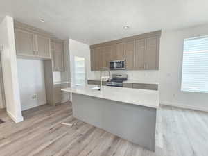 Kitchen featuring appliances with stainless steel finishes, light wood-style floors, light countertops, a center island with sink, and recessed lighting
