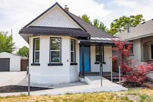 View of front of house featuring a chimney, an outbuilding, a porch, stucco siding, and a detached garage
