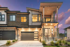 Contemporary home featuring a balcony, a garage, driveway, and stone siding