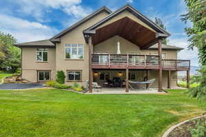 Back of property featuring stucco siding, a patio, a lawn, and a wooden deck