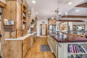 Kitchen featuring beamed ceiling, light wood finished floors, open shelves, stainless steel refrigerator with ice dispenser, and a chandelier
