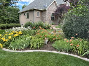 View of side of property with stucco siding, stone siding, a yard, and a shingled roof