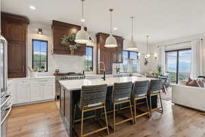 Kitchen with light countertops, a kitchen island with sink, backsplash, glass insert cabinets, and a breakfast bar area