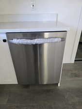 Kitchen view of dishwasher, light stone countertops, and white cabinetry