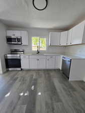 Kitchen featuring white cabinetry, appliances with stainless steel finishes, dark wood-type flooring, and a textured ceiling