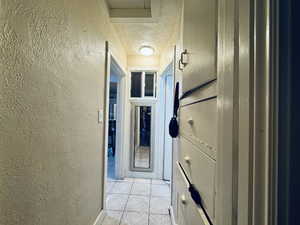 Hallway with a textured ceiling, a textured wall, and light tile patterned floors