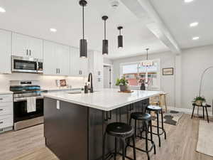 Kitchen with stainless steel appliances, light wood-type flooring, white cabinetry, a kitchen bar, and an island with sink