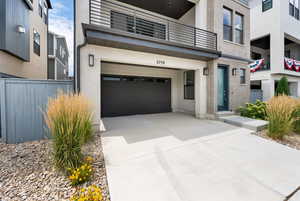 Entrance to property featuring driveway, a garage, brick siding, and a balcony