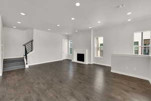 Unfurnished living room with recessed lighting, healthy amount of natural light, dark wood finished floors, and a fireplace with raised hearth