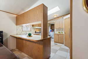 Kitchen with vaulted ceiling, a peninsula, light countertops, white range, and a skylight
