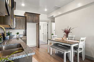 Kitchen with dark brown cabinetry, light wood-type flooring, light stone counters, recessed lighting, and stove