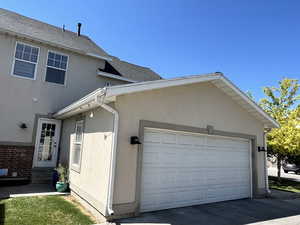 View of side of home with stucco siding, roof with shingles, a garage, and concrete driveway