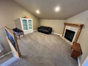 Living area featuring lofted ceiling, carpet flooring, and a tiled fireplace