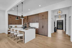 Kitchen featuring light countertops, light wood finished floors, an island with sink, a kitchen breakfast bar, and decorative light fixtures