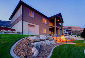 Rear view of house featuring an outdoor fire pit, a balcony, a yard, and a mountain view
