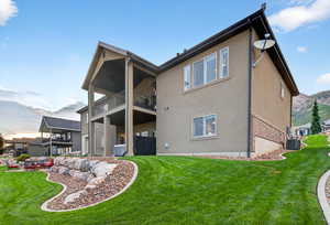 Back of property with brick siding, a yard, a balcony, and stucco siding