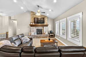 Carpeted living room with ceiling fan, lofted ceiling, and a stone fireplace