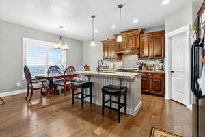 Kitchen with backsplash, wood finished floors, an island with sink, a kitchen breakfast bar, and recessed lighting