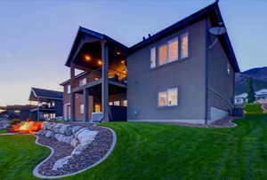 Back of property featuring a balcony, a fire pit, stucco siding, and a yard