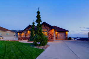 Craftsman-style home featuring stone siding, driveway, an attached garage, and a lawn