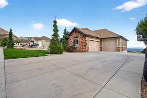 View of side of home featuring an attached garage, stone siding, concrete driveway, and a lawn