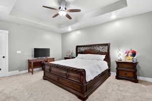 Bedroom featuring light colored carpet, a raised ceiling, recessed lighting, and ceiling fan