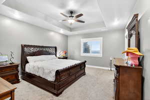 Bedroom featuring a raised ceiling, light colored carpet, and ceiling fan