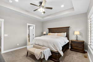 Bedroom featuring light colored carpet, a tray ceiling, a ceiling fan, ensuite bath, and recessed lighting
