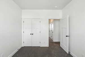 Unfurnished bedroom featuring dark carpet and a closet