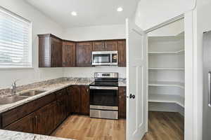 Kitchen with appliances with stainless steel finishes, light wood-style floors, dark brown cabinetry, and light stone countertops
