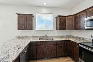 Kitchen with appliances with stainless steel finishes, light wood finished floors, dark brown cabinets, light stone countertops, and recessed lighting
