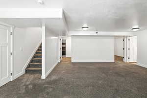 Finished basement featuring carpet flooring, stairway, and a textured ceiling