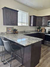 Kitchen with dark brown cabinets, a peninsula, a breakfast bar, light stone countertops, and appliances with stainless steel finishes