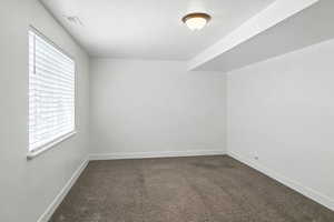 Spare room featuring dark colored carpet and plenty of natural light
