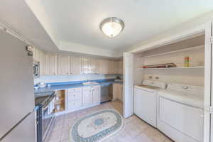 Washroom with washing machine and clothes dryer and light tile patterned flooring