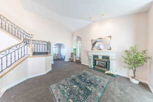 Living room with carpet, arched walkways, a tiled fireplace, stairs, and high vaulted ceiling