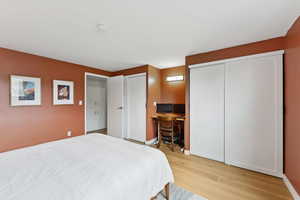 Primary bedroom with multiple closets, light real hardwood floors,and a desk