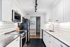 Kitchen with stainless steel appliances, white cabinetry,  tile flooring, backsplash, and stone counters